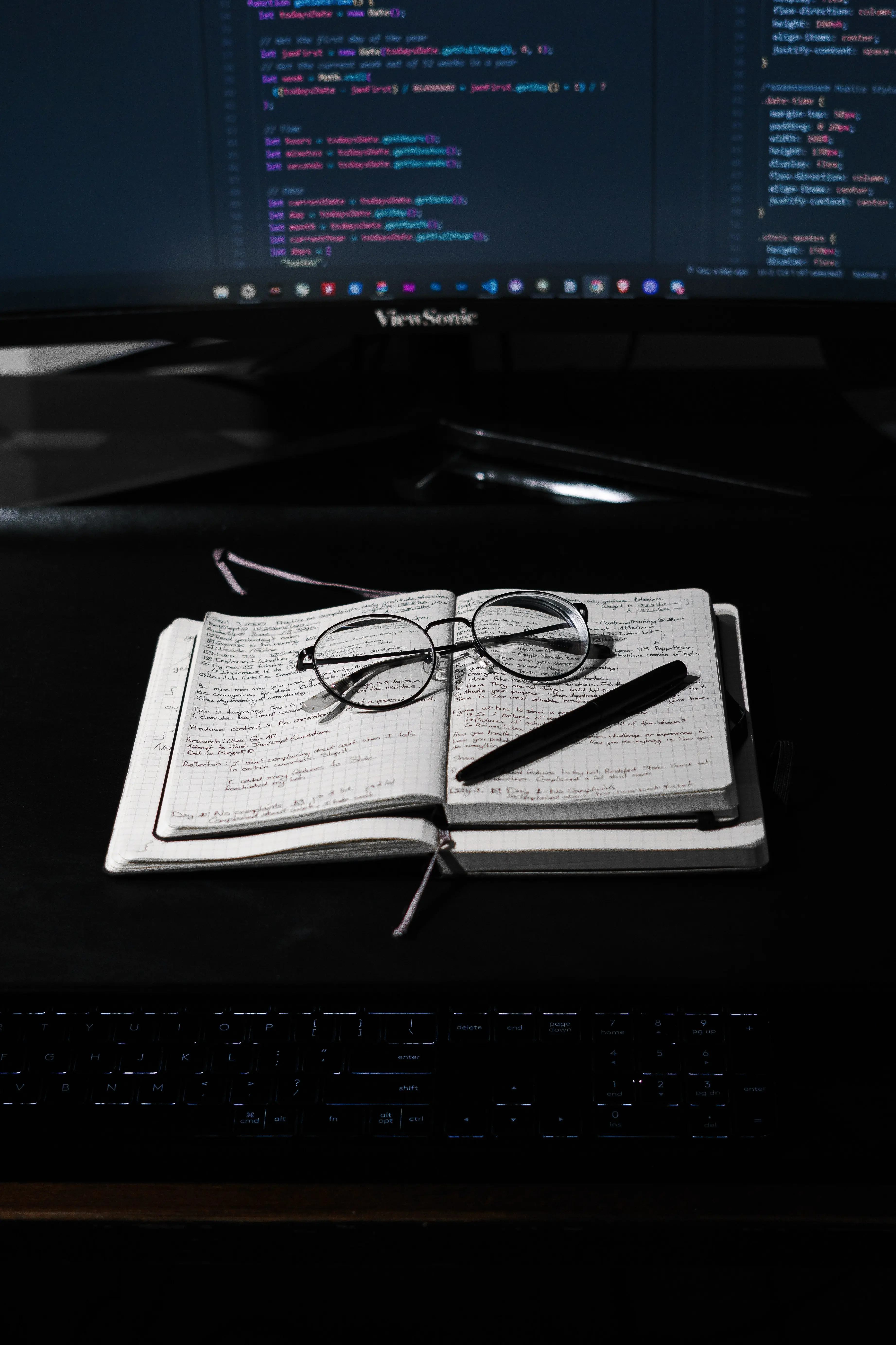 Keyboard, Notizbuch mit Brillengläsern, großer Computermonitor im hintergrund